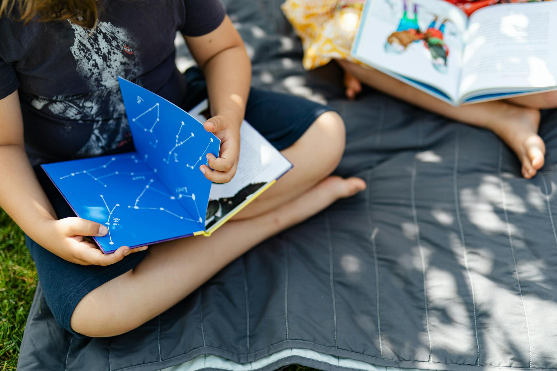 Two children reading constellation and storybooks on a sunny day outdoors.