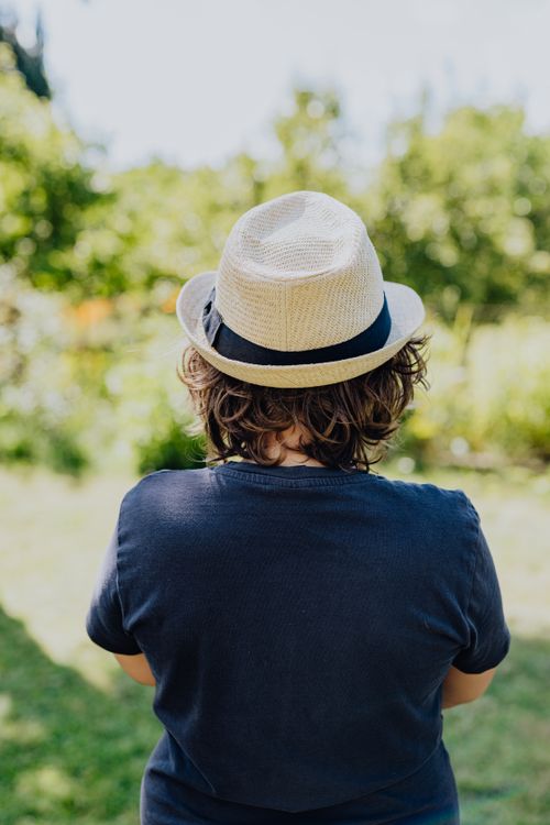 Free Back view of a boy wearing a fedora, enjoying a sunny day outdoors. Stock Photo