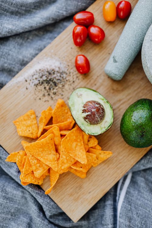 Free Top view of fresh guacamole ingredients including avocado, tomatoes, and chips on a wooden board. Stock Photo