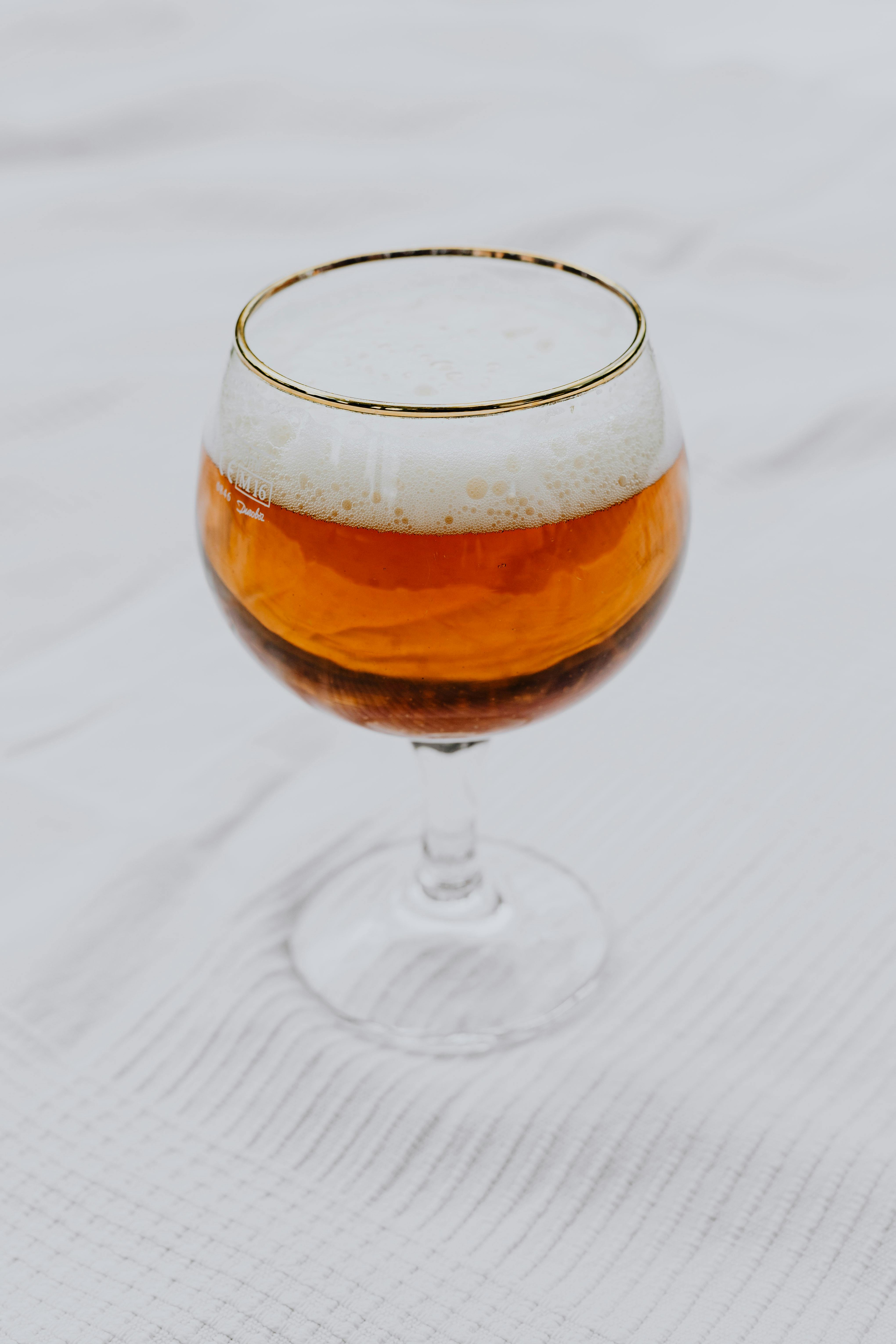 Close-up of a frothy beer served in a stylish glass with a white textured background.