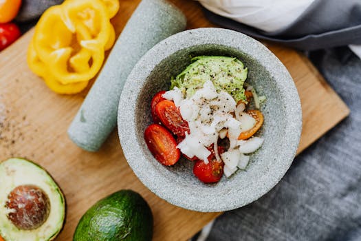 Overhead view of fresh guacamole ingredients including avocado, cherry tomatoes, and onion in a mortar and pestle.