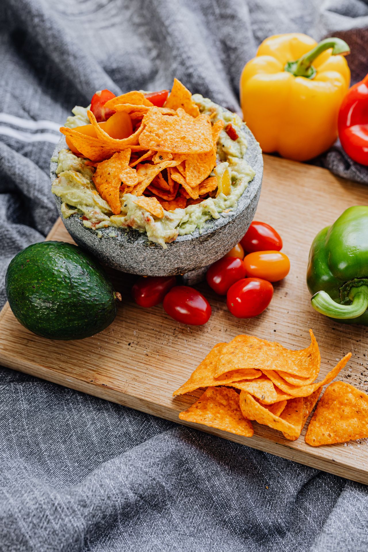 Guacamole with tortilla chips, peppers, and tomatoes on a wooden board