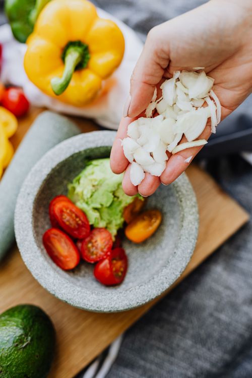 Free Hand adding onions to guacamole with tomatoes and peppers in a molcajete, top view. Stock Photo
