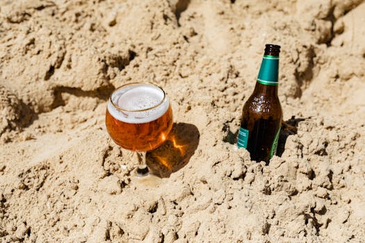 A refreshing beer glass and bottle in sandy beach setting.