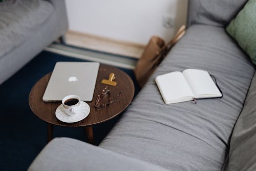 Macbook Air on Brown Wooden Table and Notebook on Gray Couch