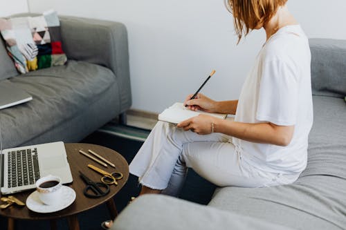 Woman in White T-shirt and White Denim Jeans Sitting on Gray Sofa