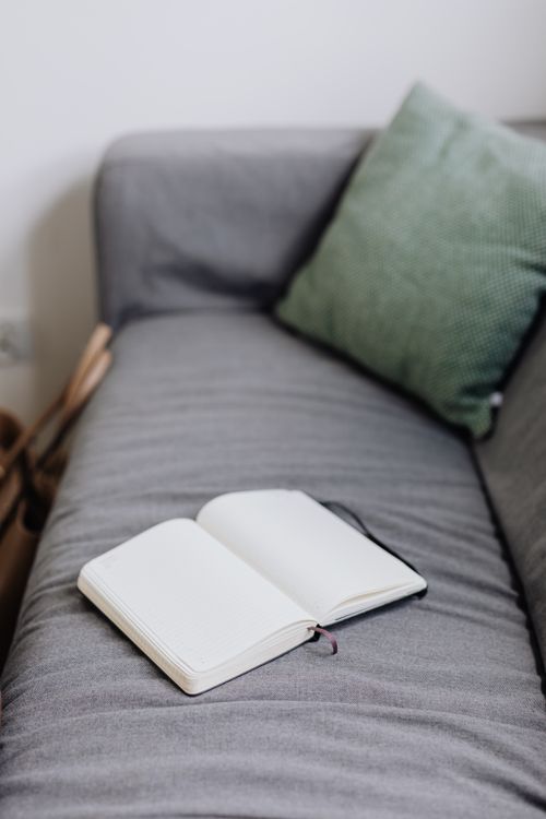 Free An open notebook placed on a gray sofa with a green pillow, ideal for relaxation or studying. Stock Photo