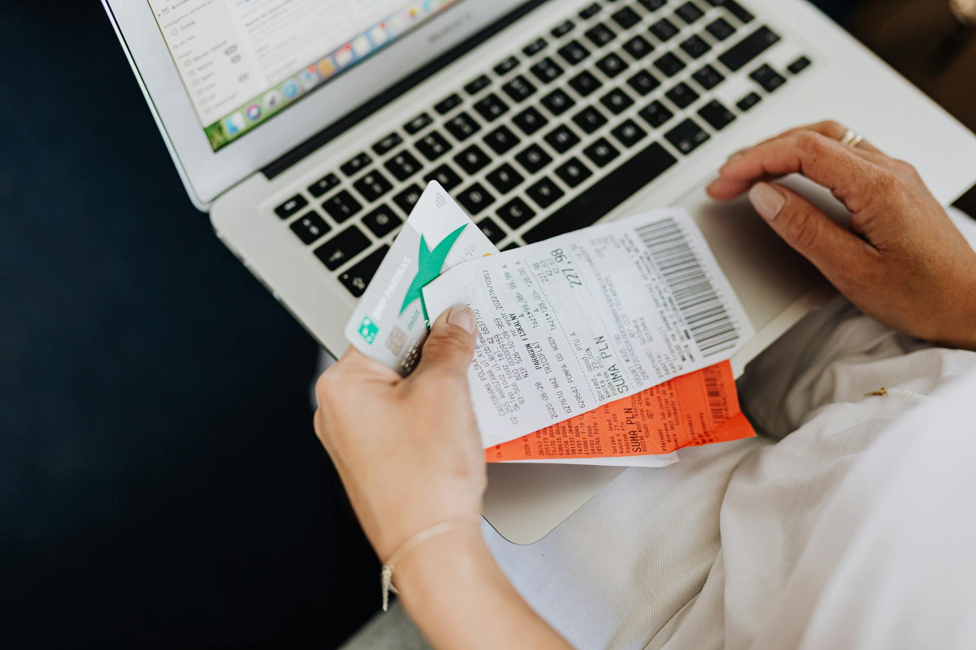 Close-up of hands holding receipts and a bank card in front of a laptop, representing online shopping and e-commerce.