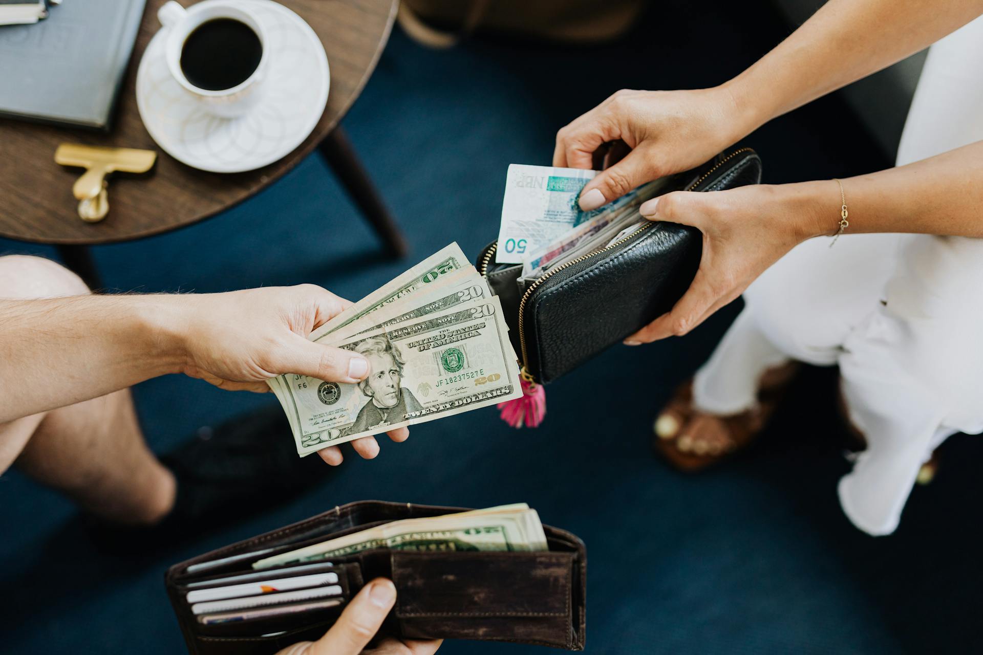 Close-up of two people exchanging US dollars and currency with wallets on a table.