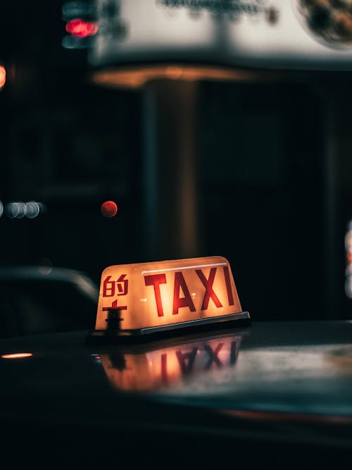 Free Illuminated taxi sign on roof of car driving on city street in evening Stock Photo