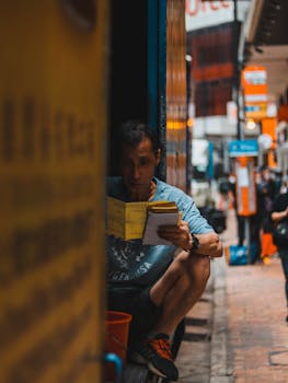Concentrated adult ethnic male worker in casual clothes reading documents while sitting in delivery truck parked on city street