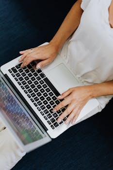 Person using a laptop indoors with focus on hands typing from above view.
