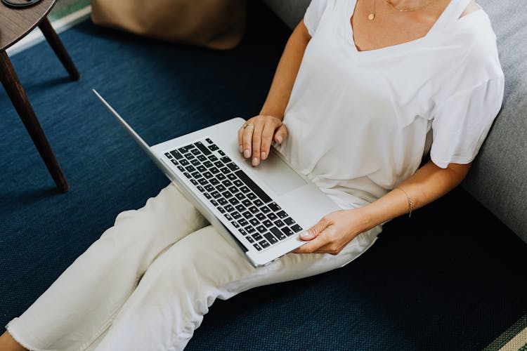 Person In White V Neck Shirt And White Pants Sitting On Blue Carpet Using Macbook Air