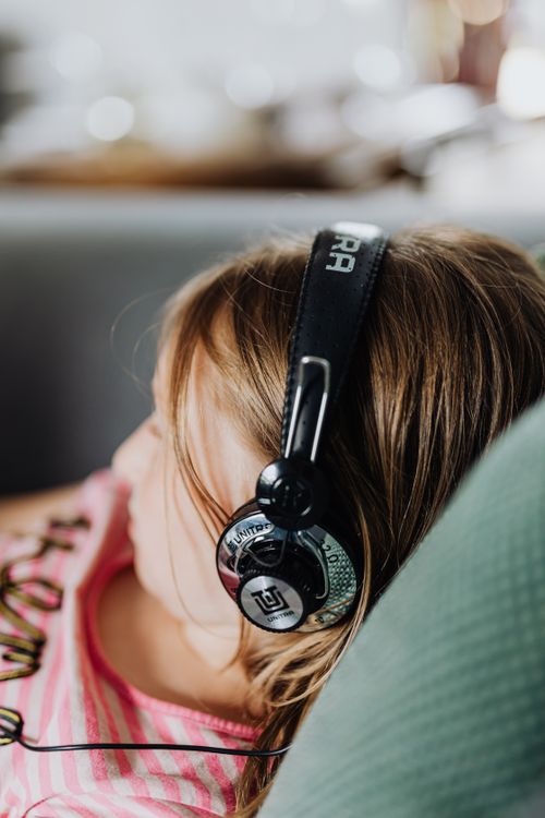 Free Close-up of a young girl wearing headphones, enjoying music indoors, relaxing on a couch. Stock Photo