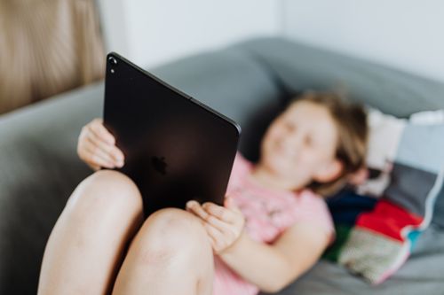 Free Young girl using a tablet while relaxing on a sofa with blurred background. Stock Photo