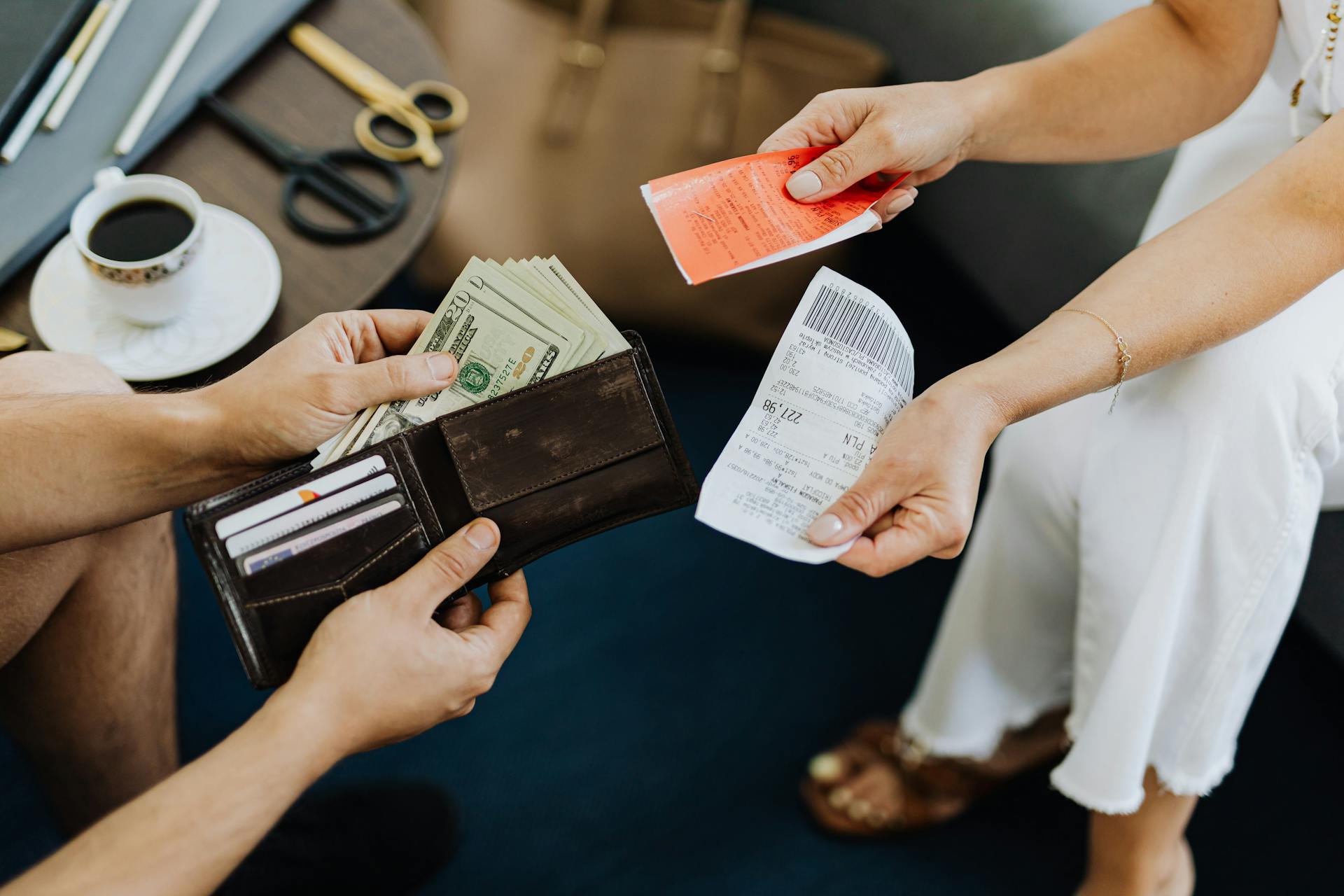 Close-up of a financial transaction involving cash and receipts over a coffee table.