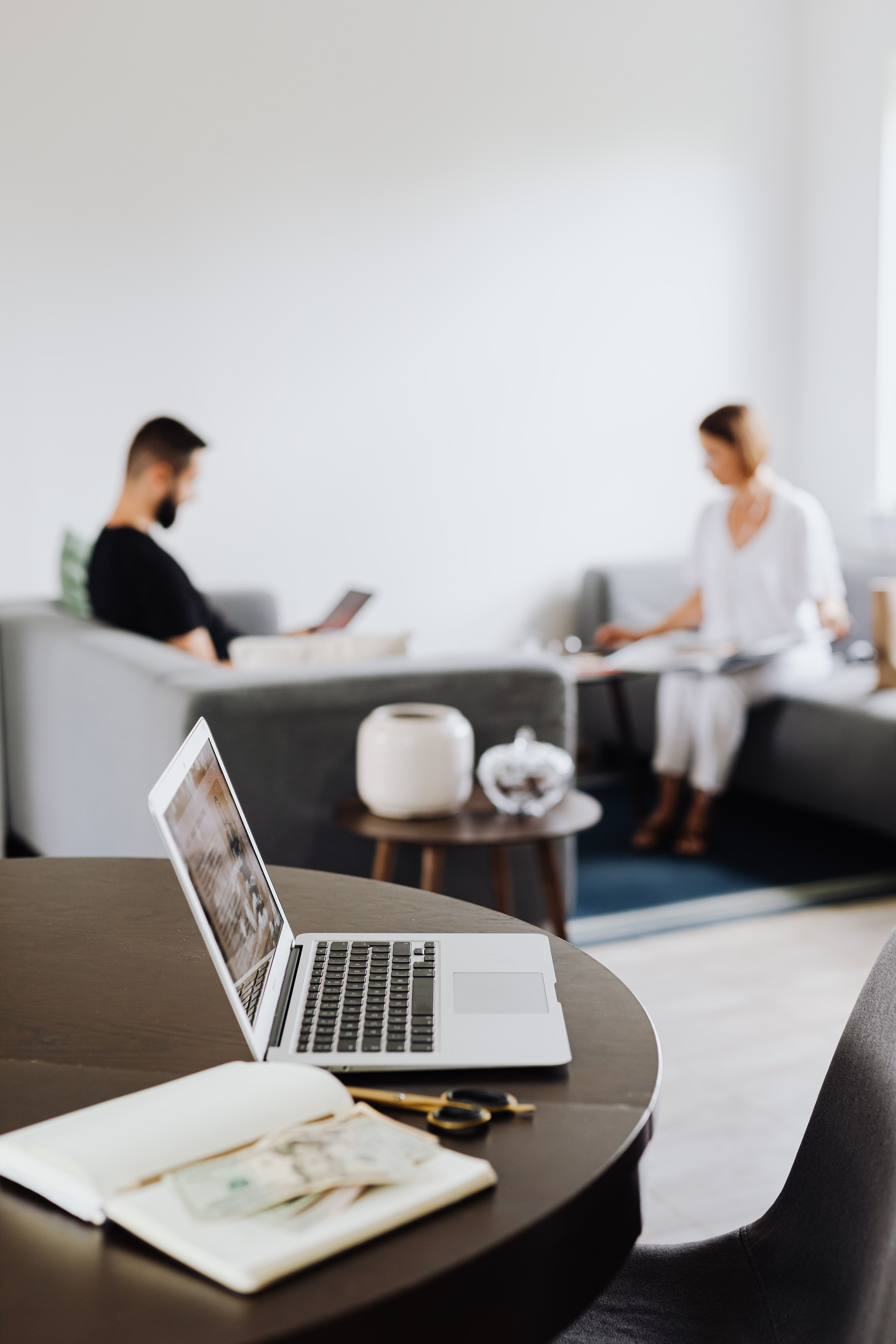 A cozy living room with a focus on a laptop, while two adults relax in the background, showcasing a modern lifestyle.
