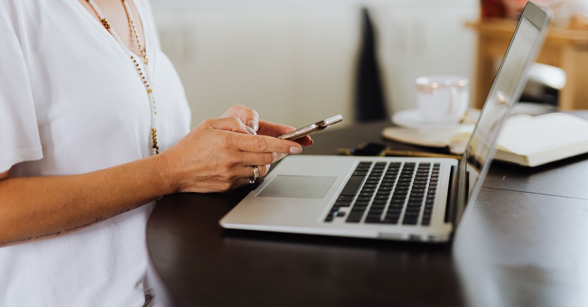person texting on phone at desk with laptop