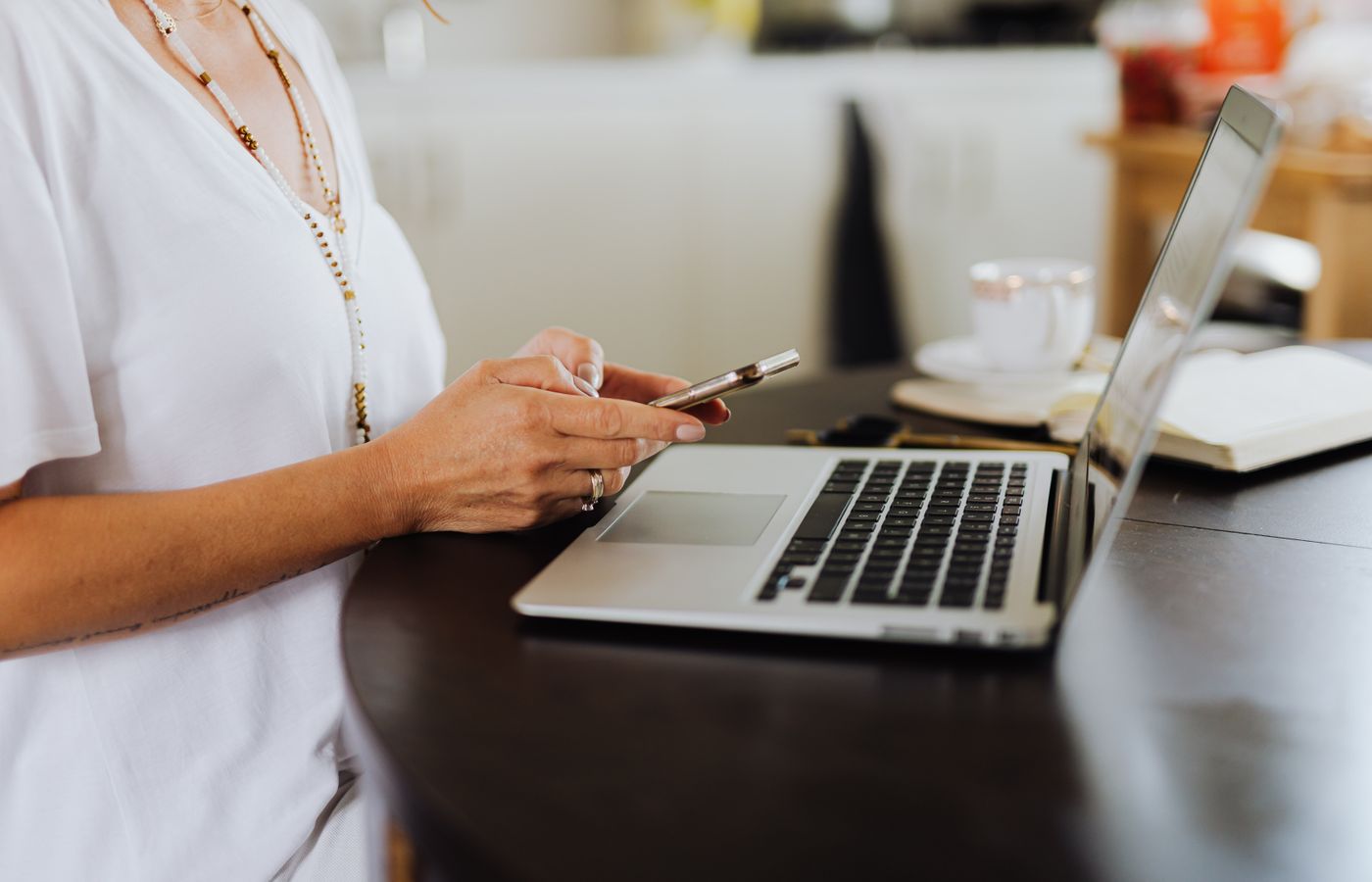 Woman engages with technology using a smartphone and laptop at a home office desk.