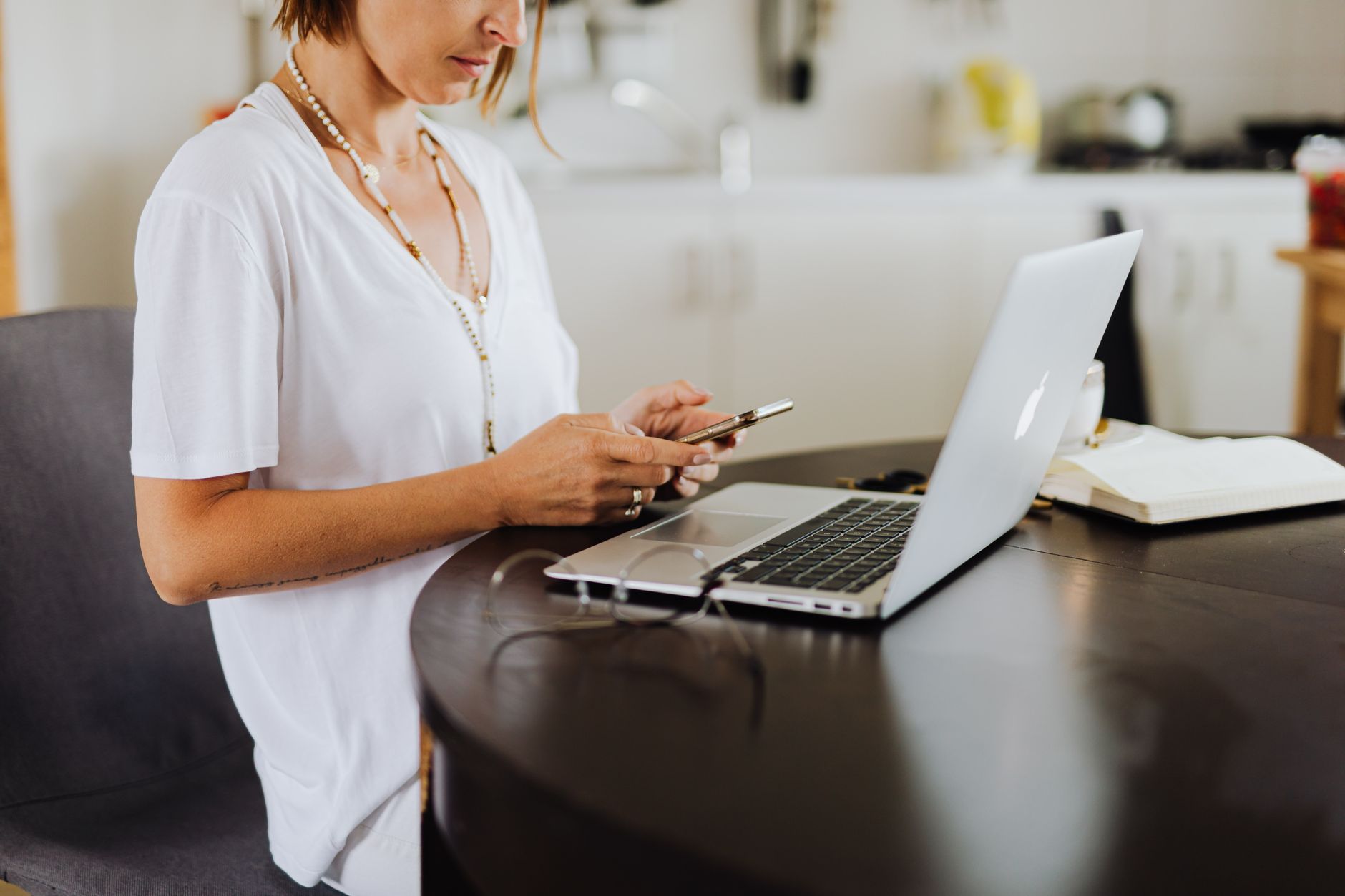 A woman at a kitchen table with a laptop and a notebook, planning a new business