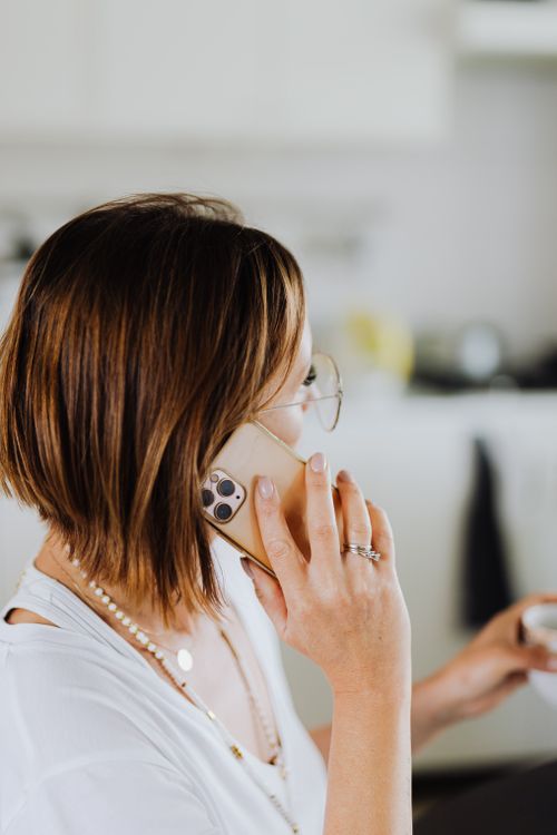 Free Rear view of an adult woman talking on a smartphone in a bright kitchen setting. Stock Photo