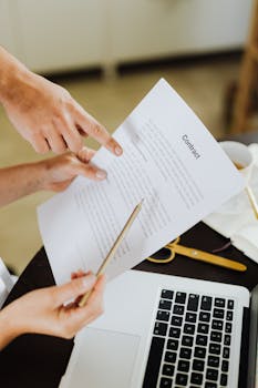 Hands pointing at contract on desk with laptop, indicating collaboration