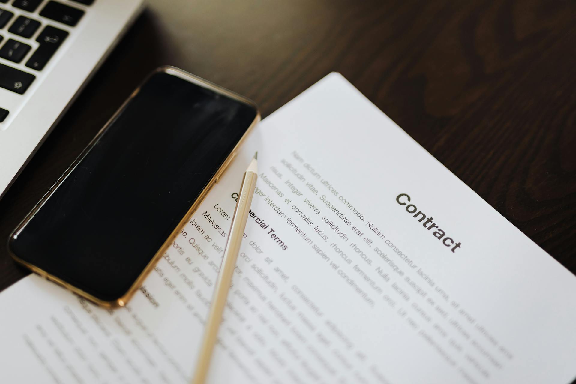 Close-up of a contract document alongside a smartphone and laptop, ideal for business concepts.