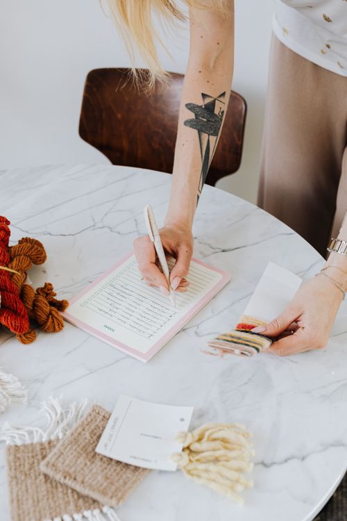 Free A person taking notes in a creative crafting workspace with yarn and fabric samples. Stock Photo