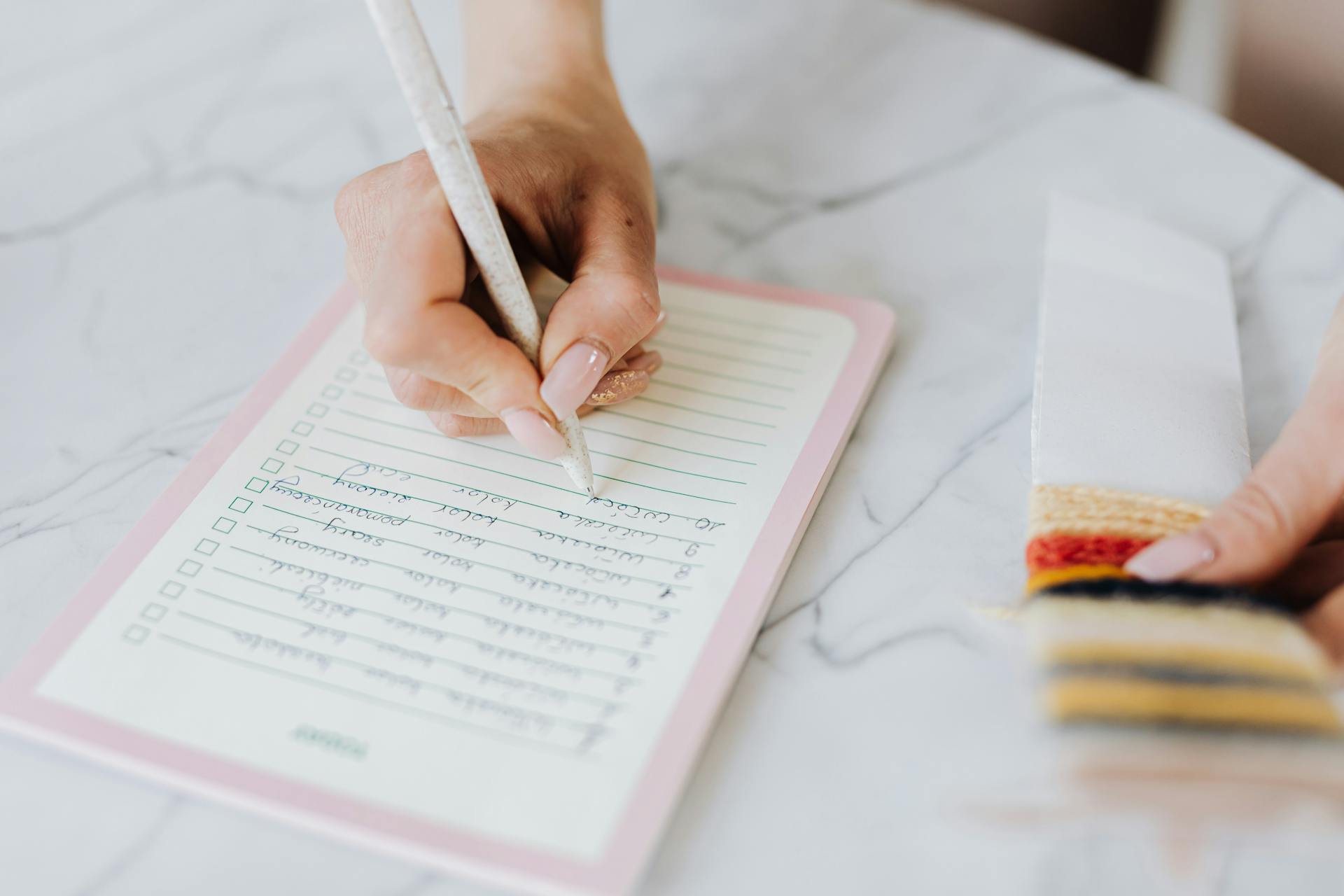 Close-up of a woman's hand writing a checklist on lined paper.