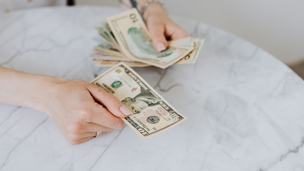 Close-up of hands counting US dollar bills on a marble table surface.