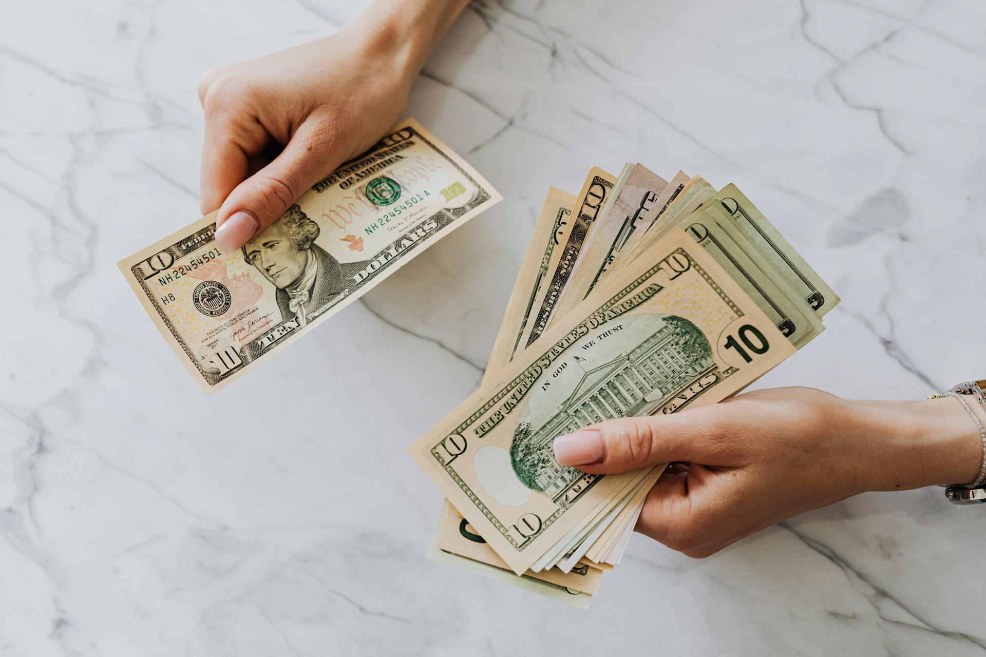 Close-up of hands counting US dollar bills on a marble background, highlighting financial theme.