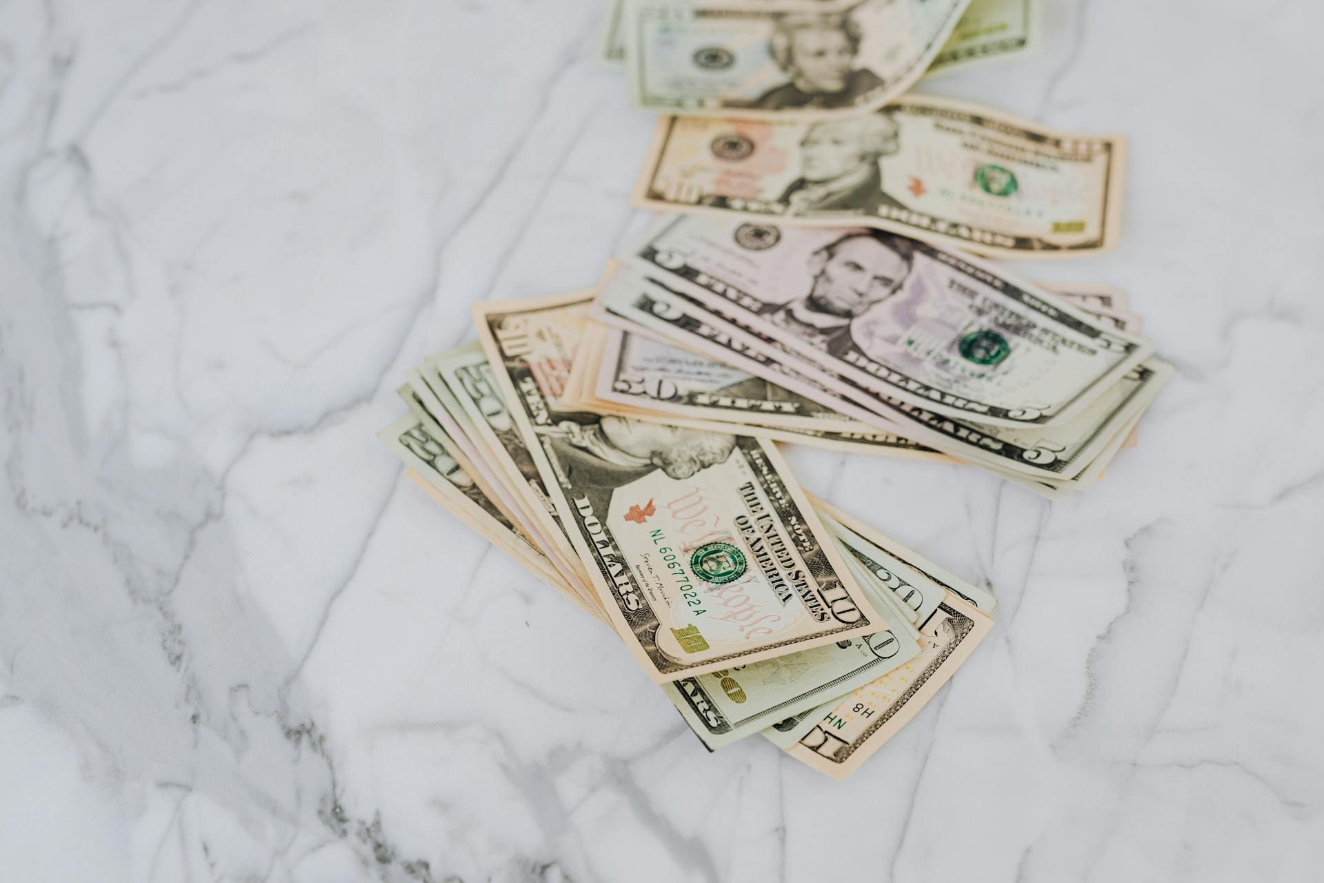 A stack of US dollar bills spread on a marble surface, representing wealth and finance.