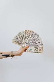 Close-up of a hand displaying fanned out US dollar bills against a white background.