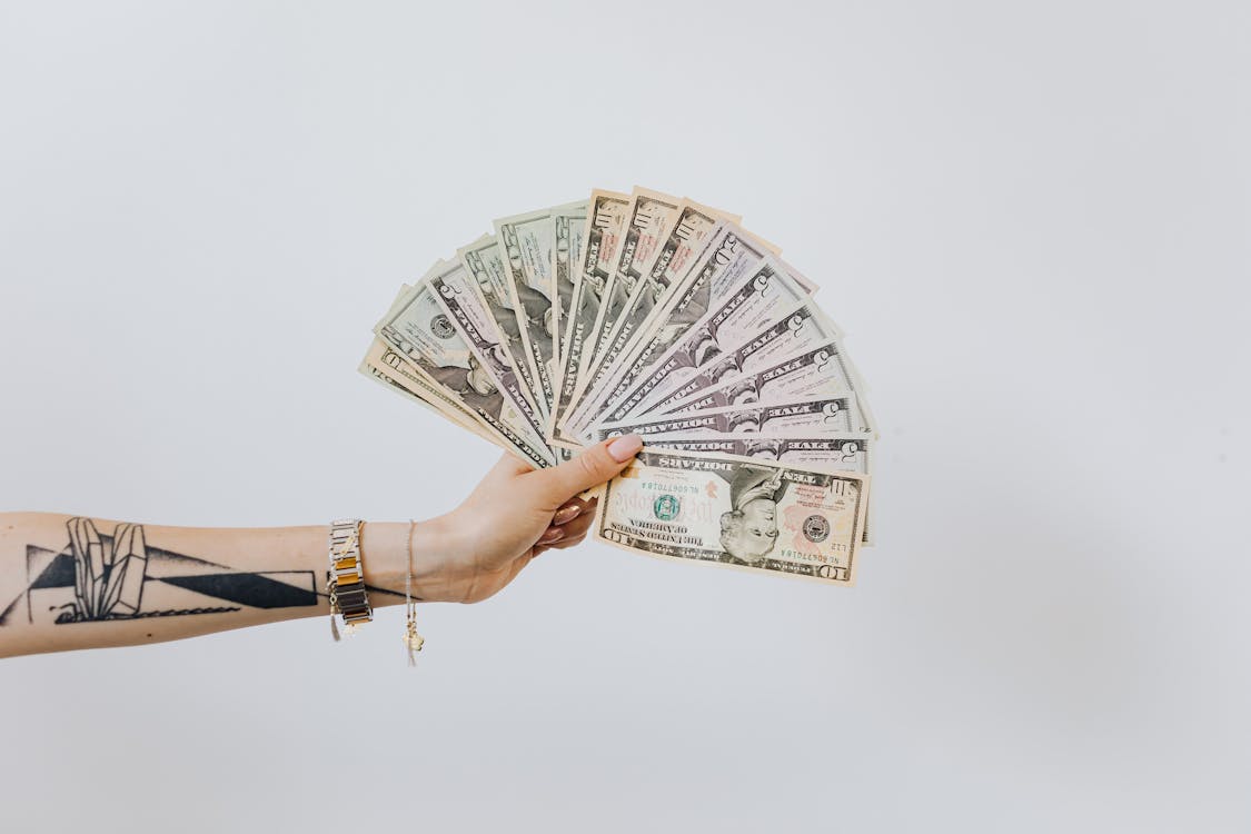 A tattooed hand holding several dollar bills