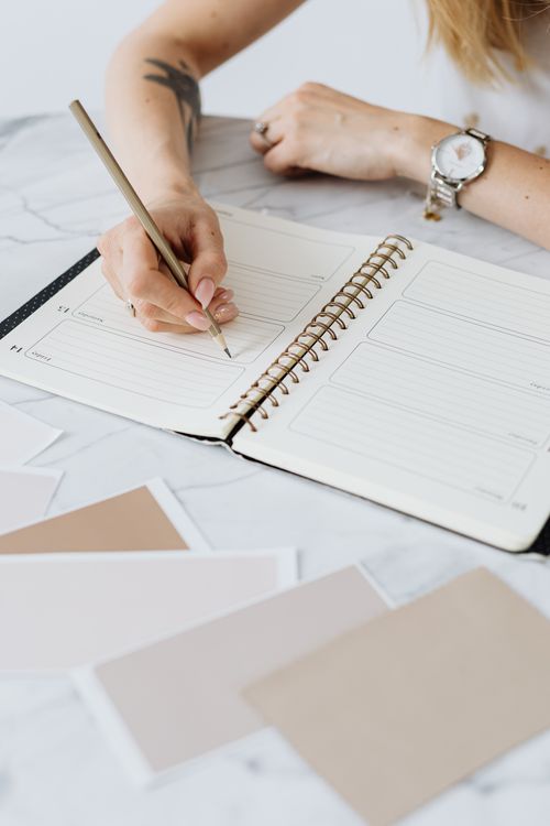 Free A woman writing notes in a spiral notebook surrounded by color swatches on a table. Stock Photo