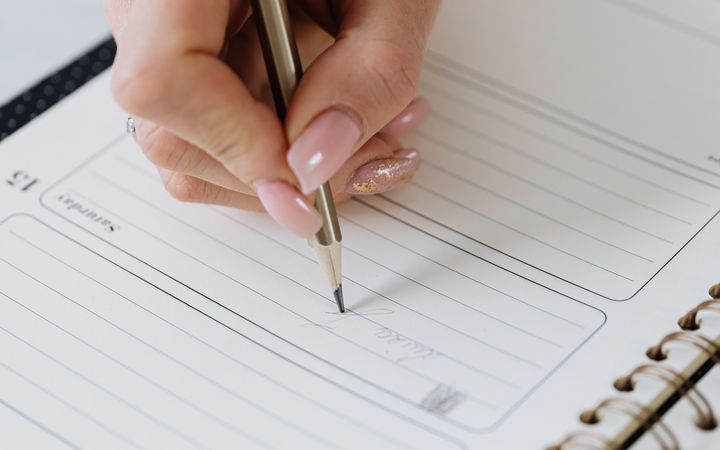 A close-up of a hand writing in a planner with a pencil. Ideal for organization themes.