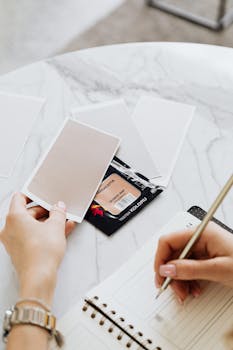 Close-up of a person writing in a notebook with blank cards on a marble table.
