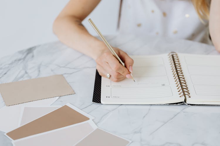 Woman With Writing In A Calendar And Beige Colour Samples On White Table