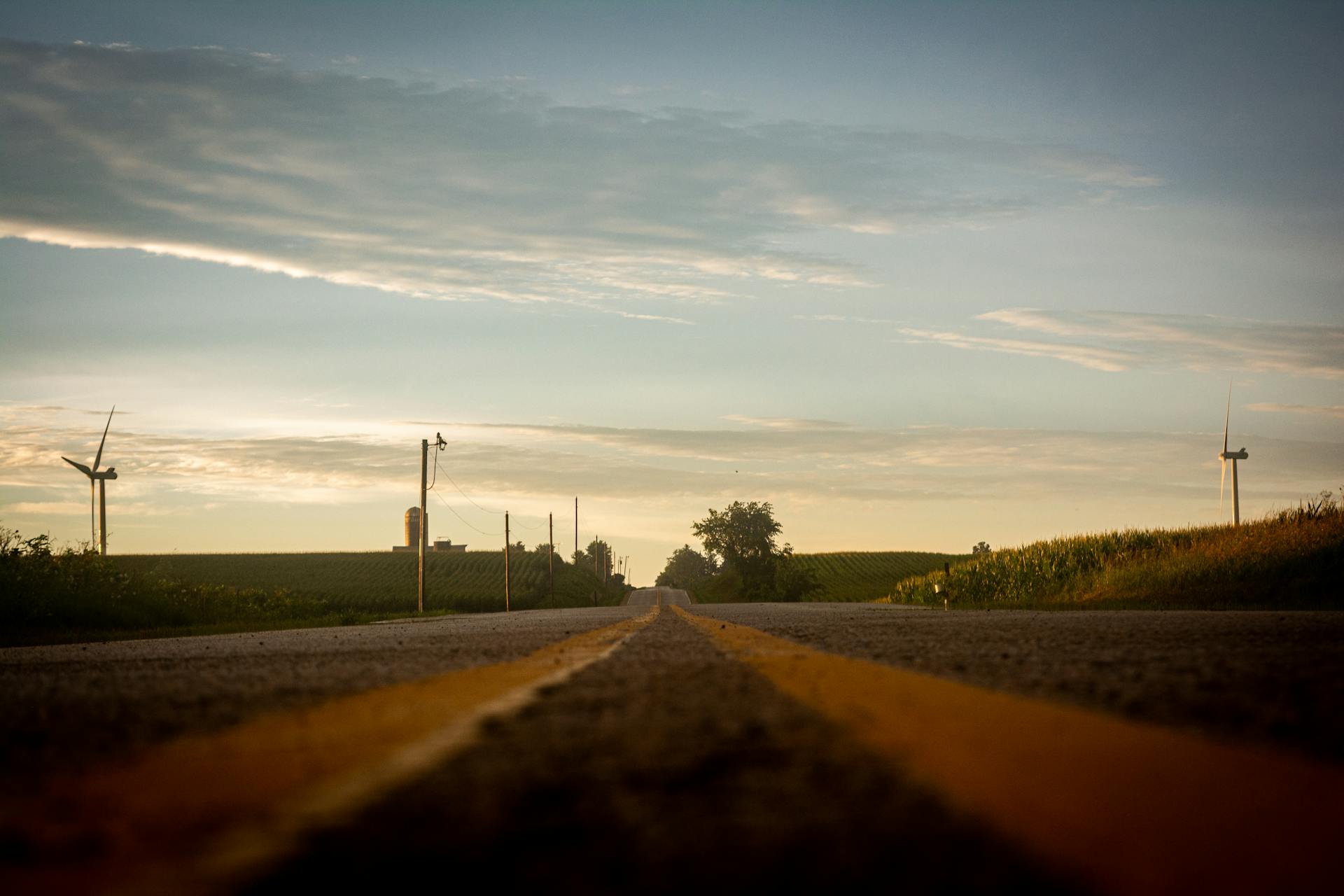 Scenic countryside road in Wisconsin at sunrise with wind turbines and farmland.