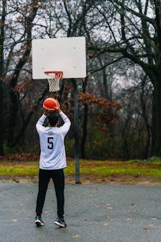 A basketball player shooting on an outdoor court surrounded by fall foliage.