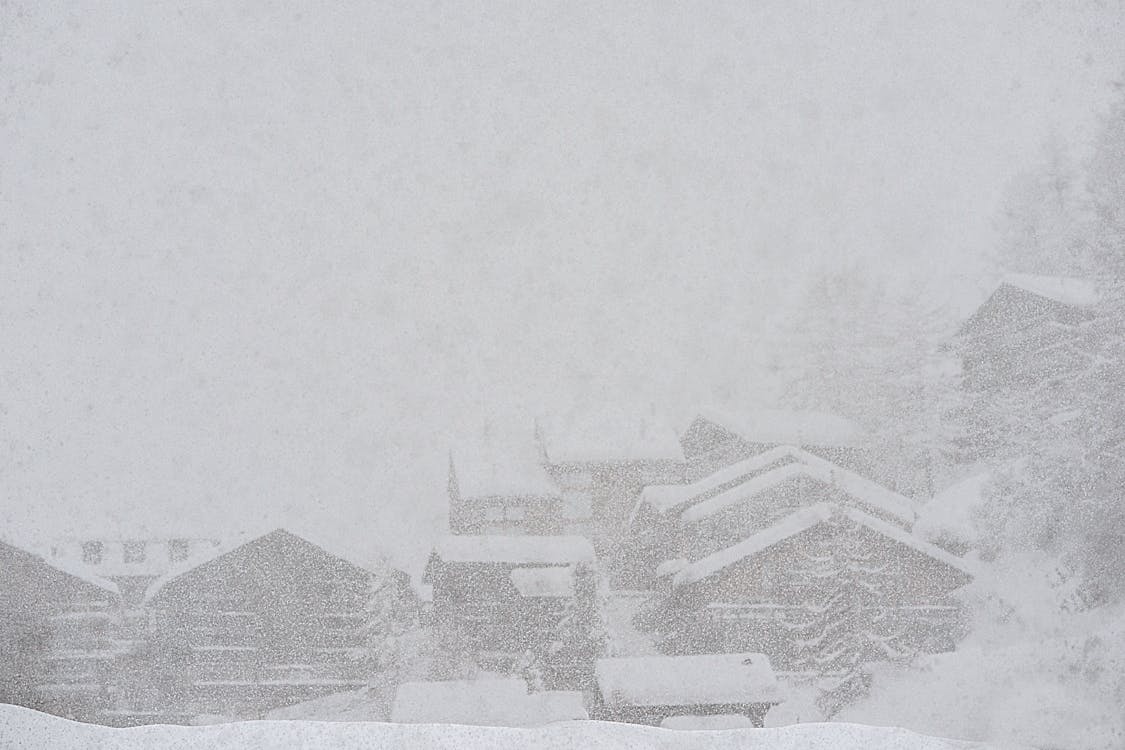 Severe scenery of remote rural village houses covered with thick layer of snow during intense snowstorm on cold winter day