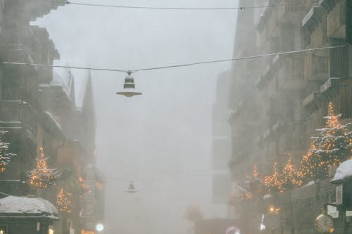 Modern frozen city street with overhanging streetlamps covered with snow on gloomy foggy winter day