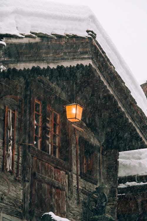 Wooden cottage with burning lantern during snowfall