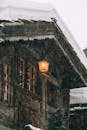 Wooden cottage with burning lantern during snowfall