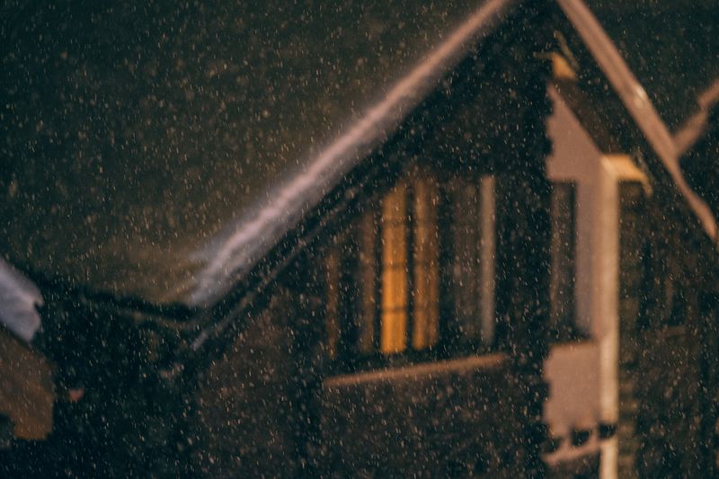 Snowy wooden cabin during a winter snowfall at night