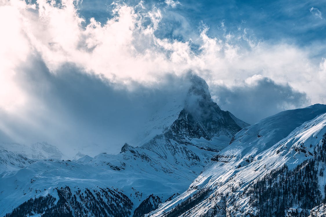 Snowy mountain peaks under cloudy sky in sunlight · Free Stock Photo