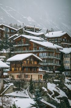 Alpine village with residential houses and buildings surrounded by massive snowy mountains on foggy day