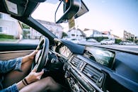 Side view of crop unrecognizable young female driver in denim jacket driving modern car on road near typical residential houses on sunny day