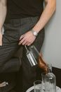 一名面目全非、穿着优雅服装、手持香槟长笛的男性站在墙边