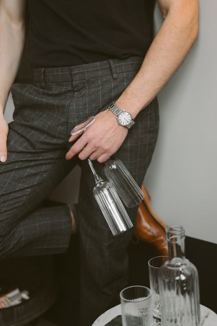 Crop unrecognizable male in elegant outfit standing near wall with pair of champagne glass flutes